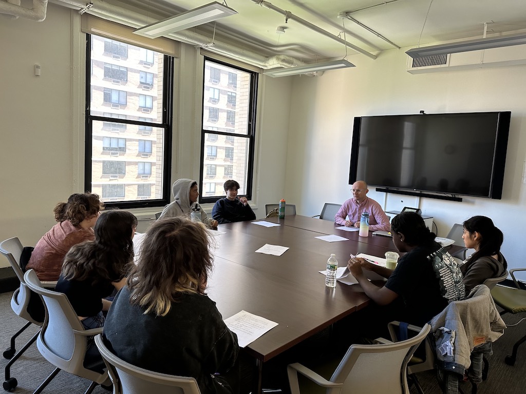 Students sit around a large conference table during a Future Dramatic Writers class.